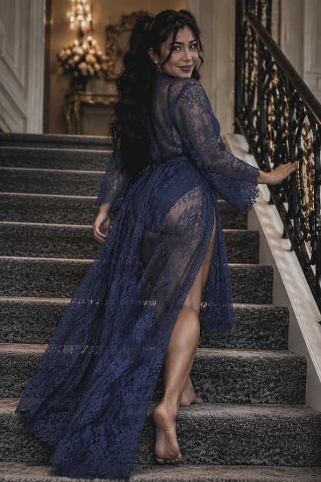 A woman in a long, navy blue lace robe walking up a carpeted staircase.